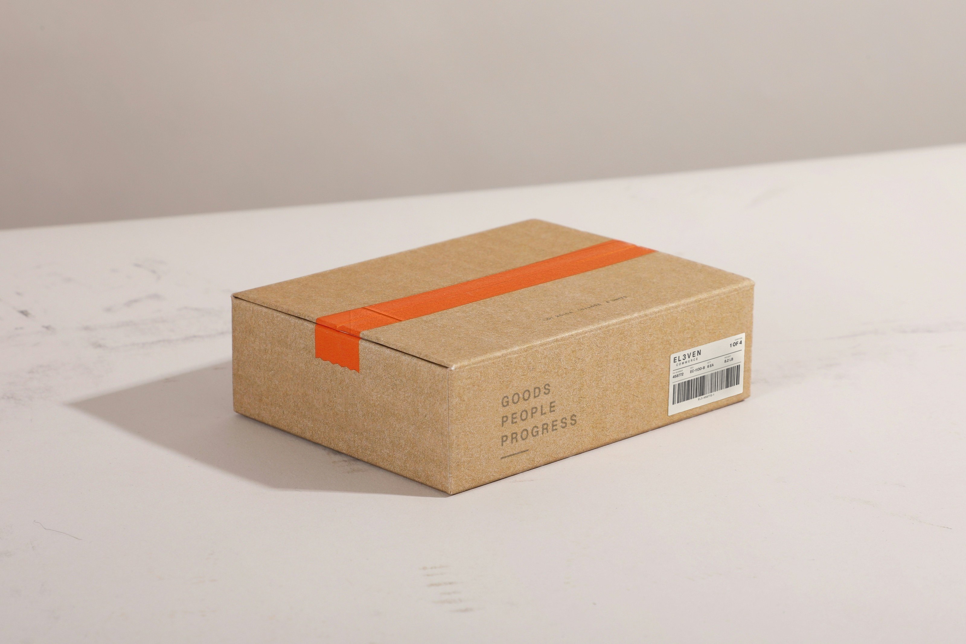 A sealed kraft carton on a pale surface with an El3ven Commerce shipping label on its side